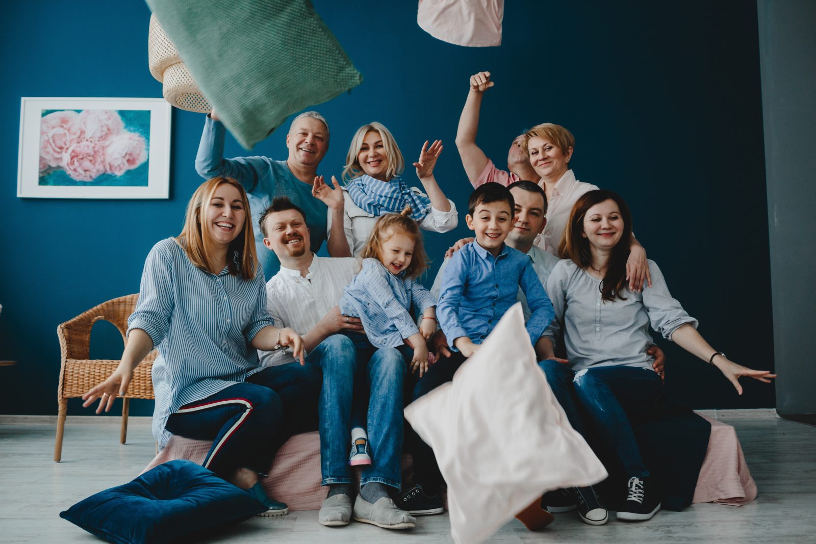 Grandparents, parents and their little children sit together on the bed in a blue room and fight pillows